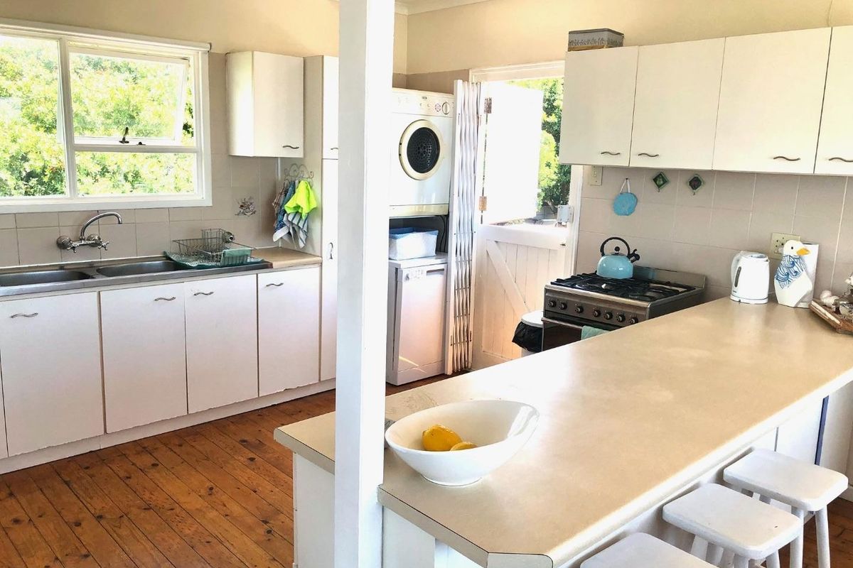 Functional kitchen featuring white cabinetry, a breakfast bar, stainless steel sink, and integrated laundry space with direct outdoor access.