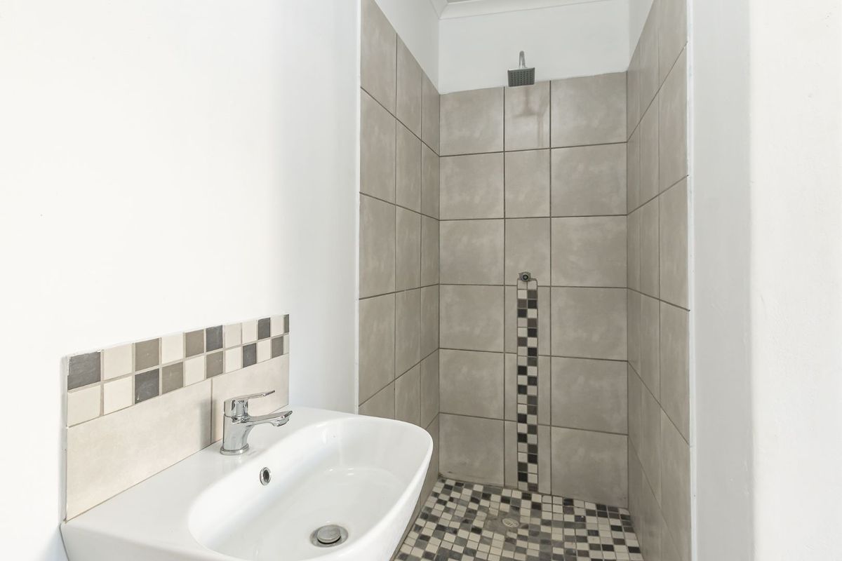 A clean bathroom featuring a walk-in shower with neutral tiling and a modern washbasin with mosaic tile backsplash.