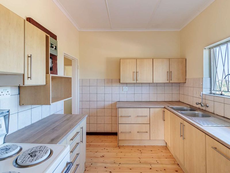A functional kitchen featuring light wood-tone cabinetry, laminate countertops, a double stainless steel sink, and tiled backsplash, set against timber flooring.