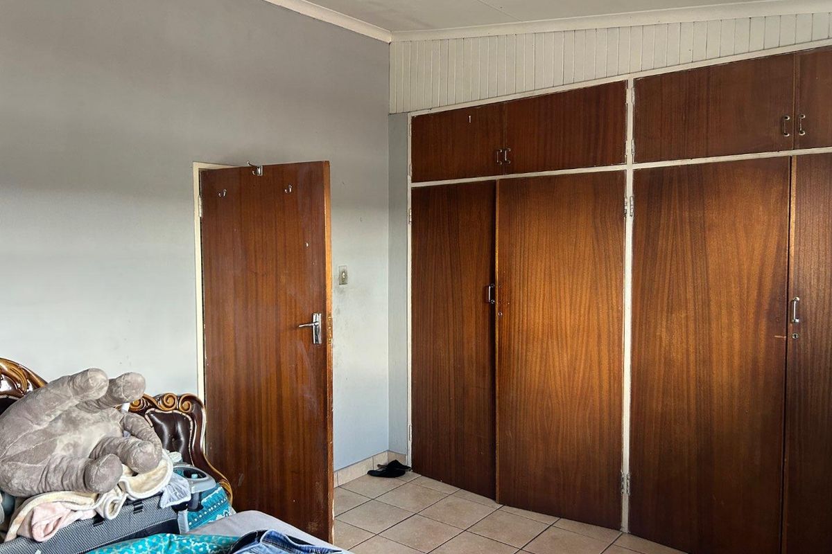 A bedroom featuring built-in wooden cupboards and tiled flooring, offering functional storage space in need of cosmetic updates.