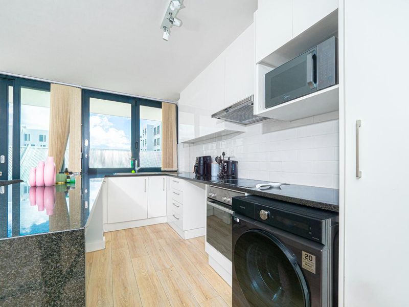 Modern kitchen featuring white cabinetry, granite countertops, subway tile backsplash, and integrated appliances, with direct access to a balcony through sliding glass doors.