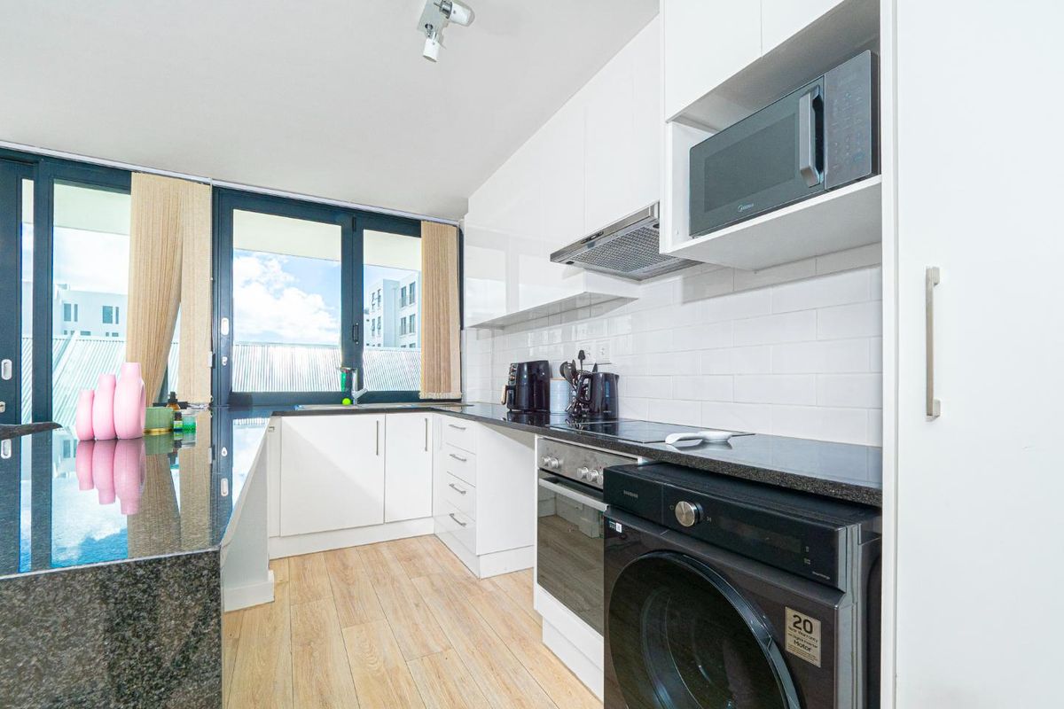 Modern kitchen featuring white cabinetry, granite countertops, subway tile backsplash, and integrated appliances, with direct access to a balcony through sliding glass doors.