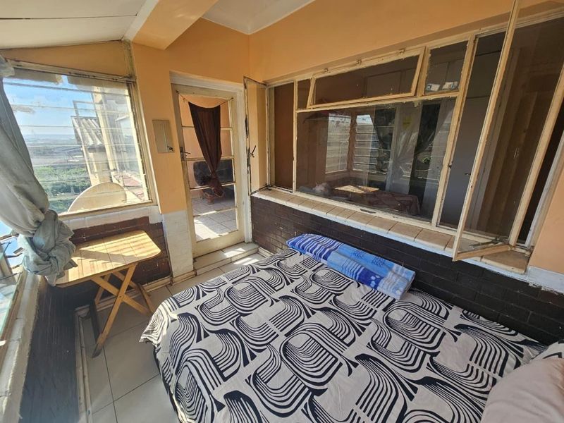 Enclosed balcony area featuring tiled flooring, brick wall accents, and large windows, offering potential for a bright sunroom or additional living space.