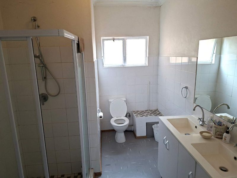 A functional bathroom featuring a shower enclosure, double vanity with built-in cabinetry, and a toilet, requiring cosmetic updates to modernize the space.