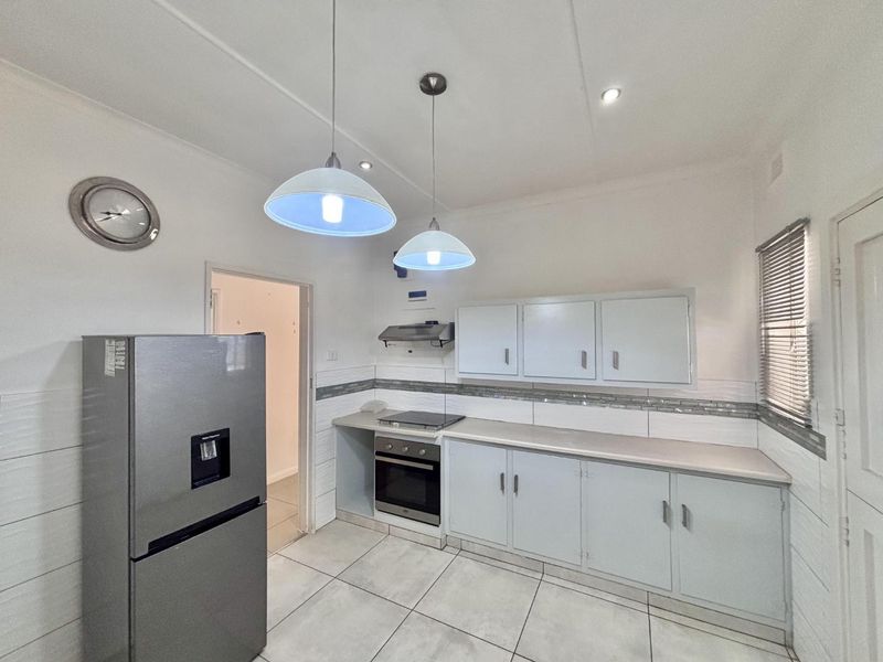 A functional kitchen featuring built-in cabinetry, laminate countertops, an electric hob, oven, extractor fan, and tiled flooring with a neutral backsplash.