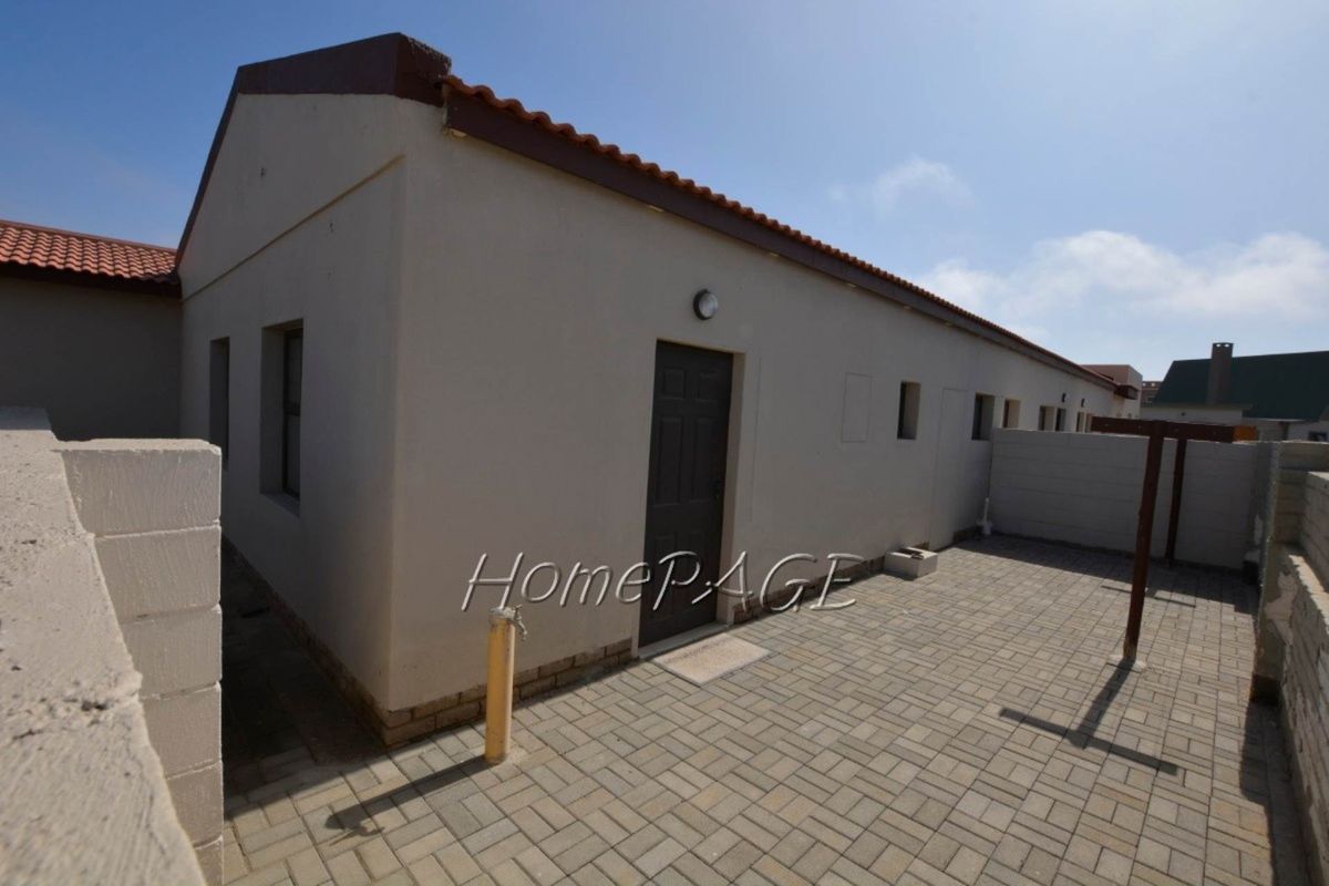 Exterior view of the rear of the property featuring paved courtyard area, brick boundary walls, and a single access door.