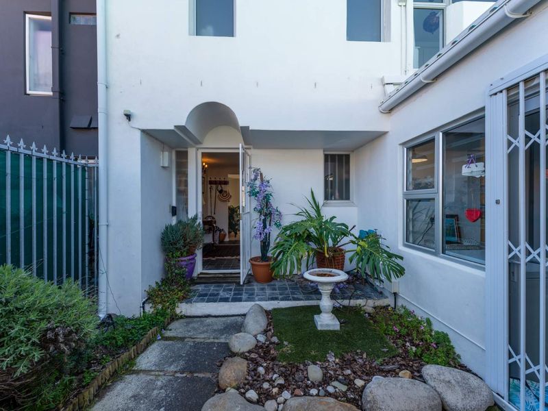 A rear exterior view of the property featuring a paved entrance area, security gate, and aluminium window frames.