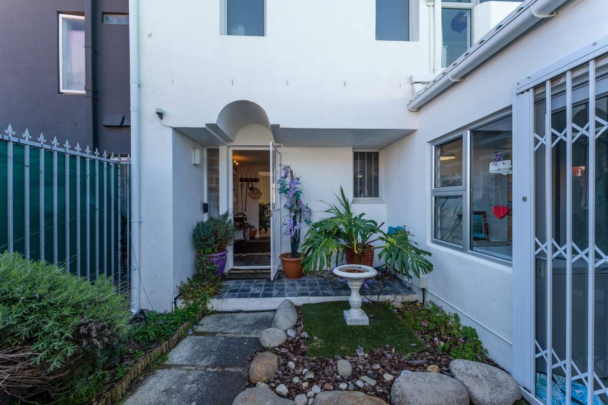 A rear exterior view of the property featuring a paved entrance area, security gate, and aluminium window frames.