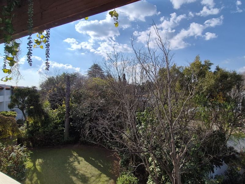 A scenic elevated view overlooking a lush garden area with mature trees and a well-maintained lawn, framed by a timber pergola structure.