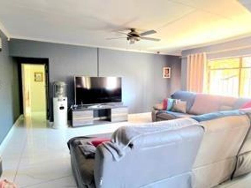 A spacious living room featuring tiled flooring, a ceiling fan, and large windows with security bars, offering a comfortable and functional living space.