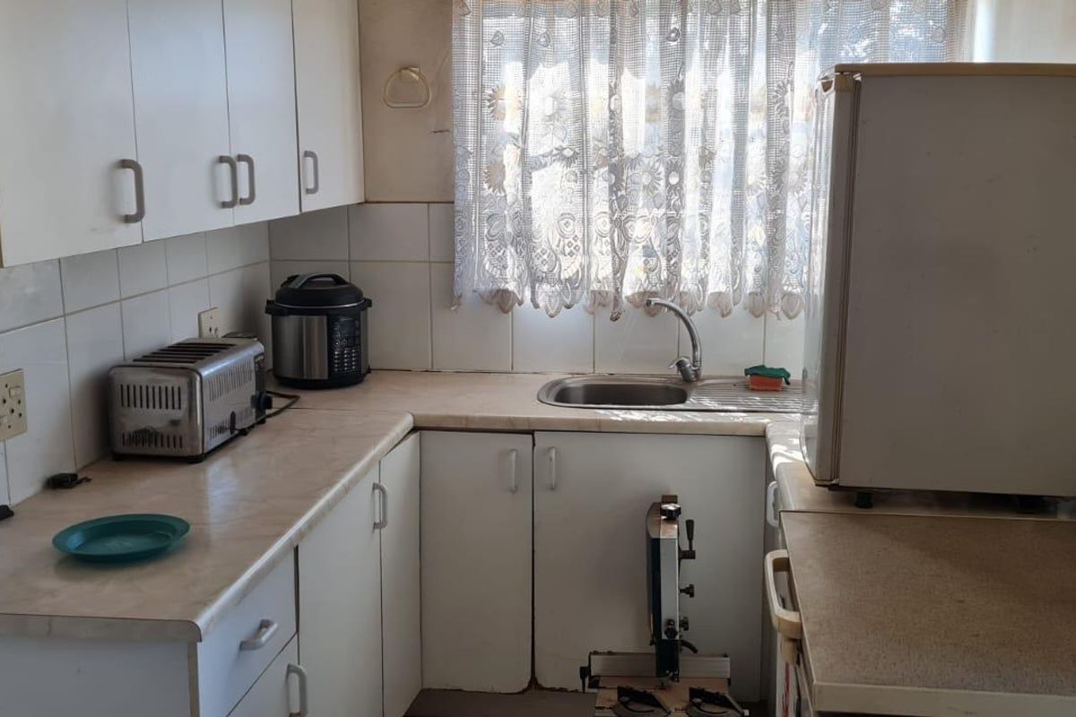 A compact kitchen featuring laminate countertops, a stainless steel sink, and tiled backsplash, requiring cosmetic updates to modernize the space.