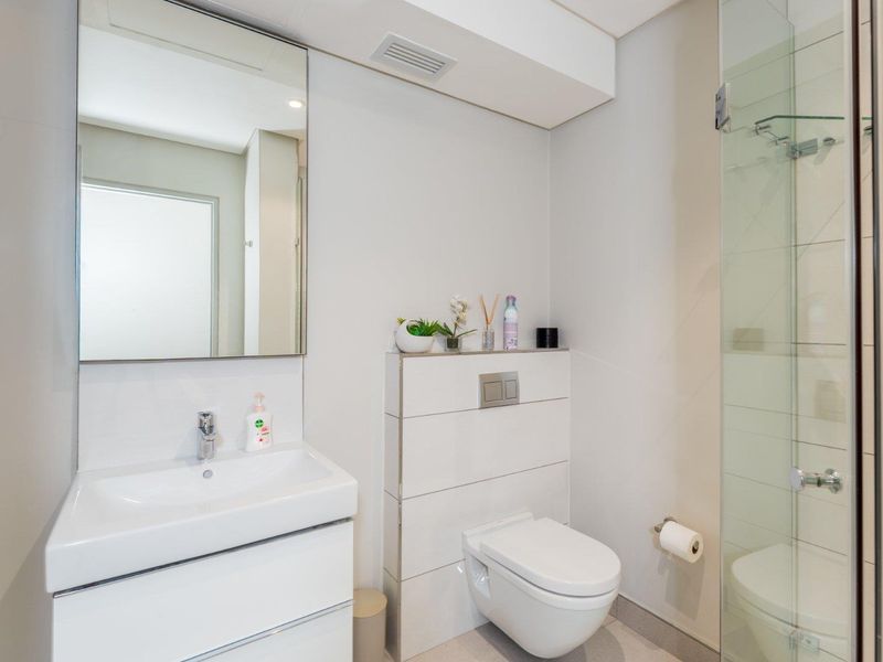 Modern bathroom featuring a wall-mounted toilet with concealed cistern, vanity basin with mixer tap, and a glass-enclosed shower.