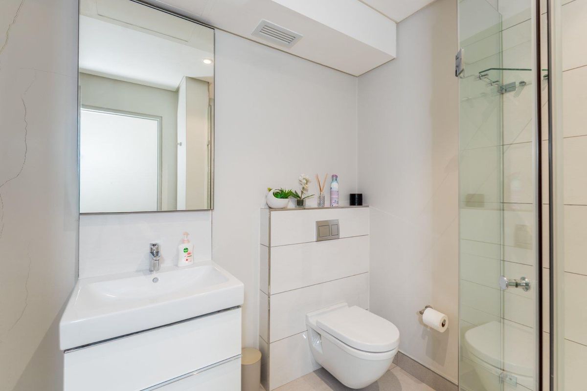Modern bathroom featuring a wall-mounted toilet with concealed cistern, vanity basin with mixer tap, and a glass-enclosed shower.