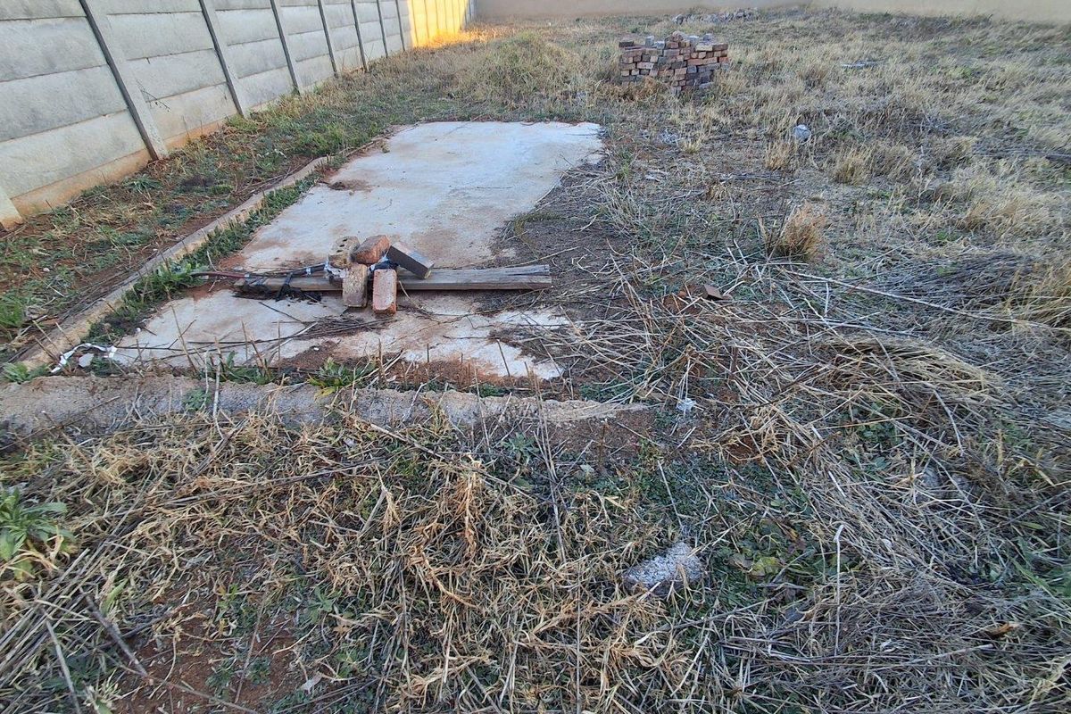 A large, undeveloped backyard area featuring a precast concrete boundary wall and an existing concrete slab foundation, requiring significant landscaping and site preparation.