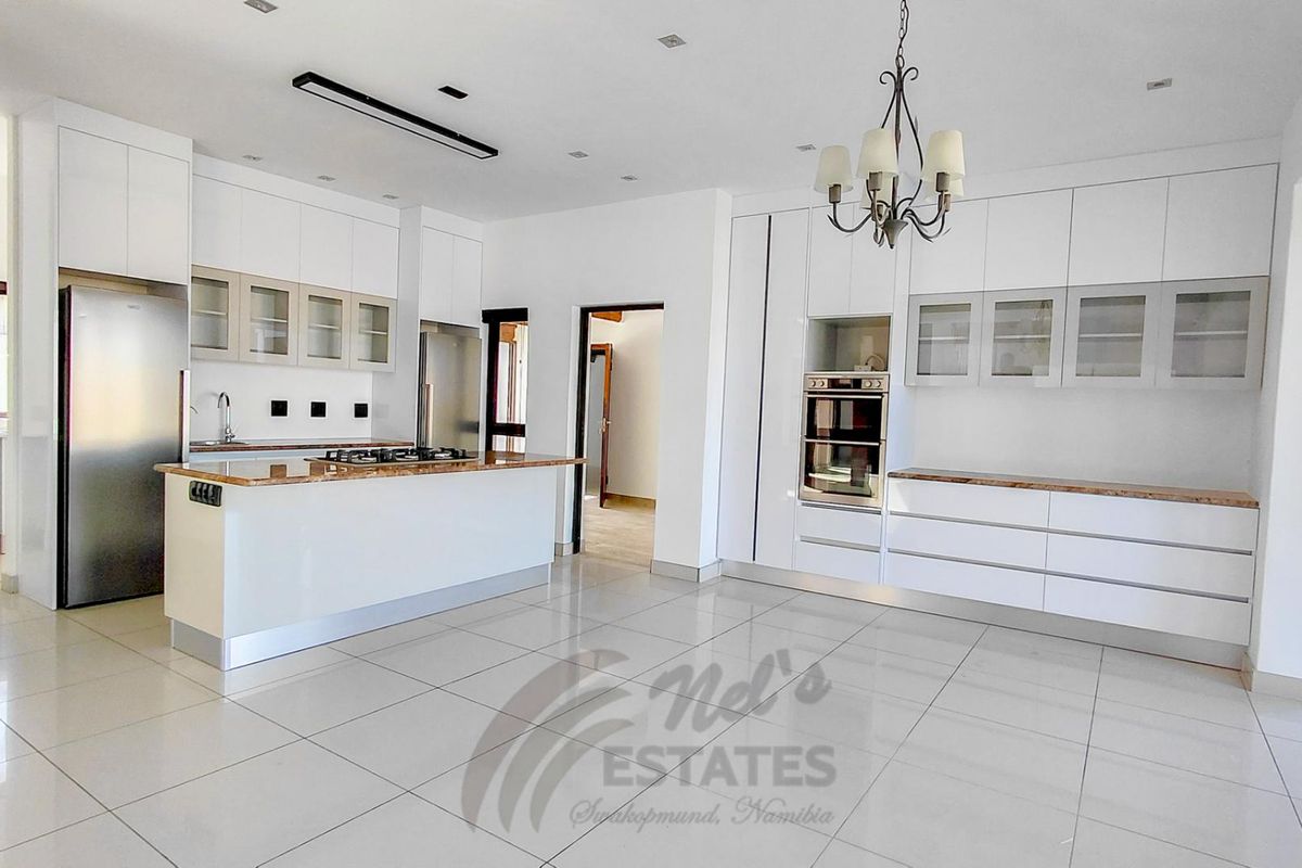 Modern kitchen featuring white cabinetry, stone countertops, a central island with a gas hob, and built-in double ovens, finished with large format floor tiles.