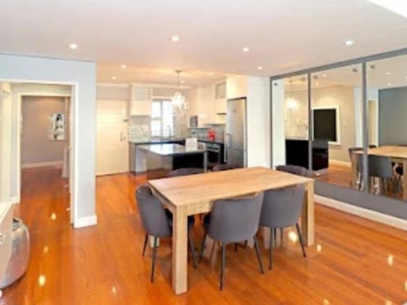 Open-plan living and dining area featuring polished hardwood flooring, recessed lighting, and a modern kitchen with a central island and mirrored wall accents.