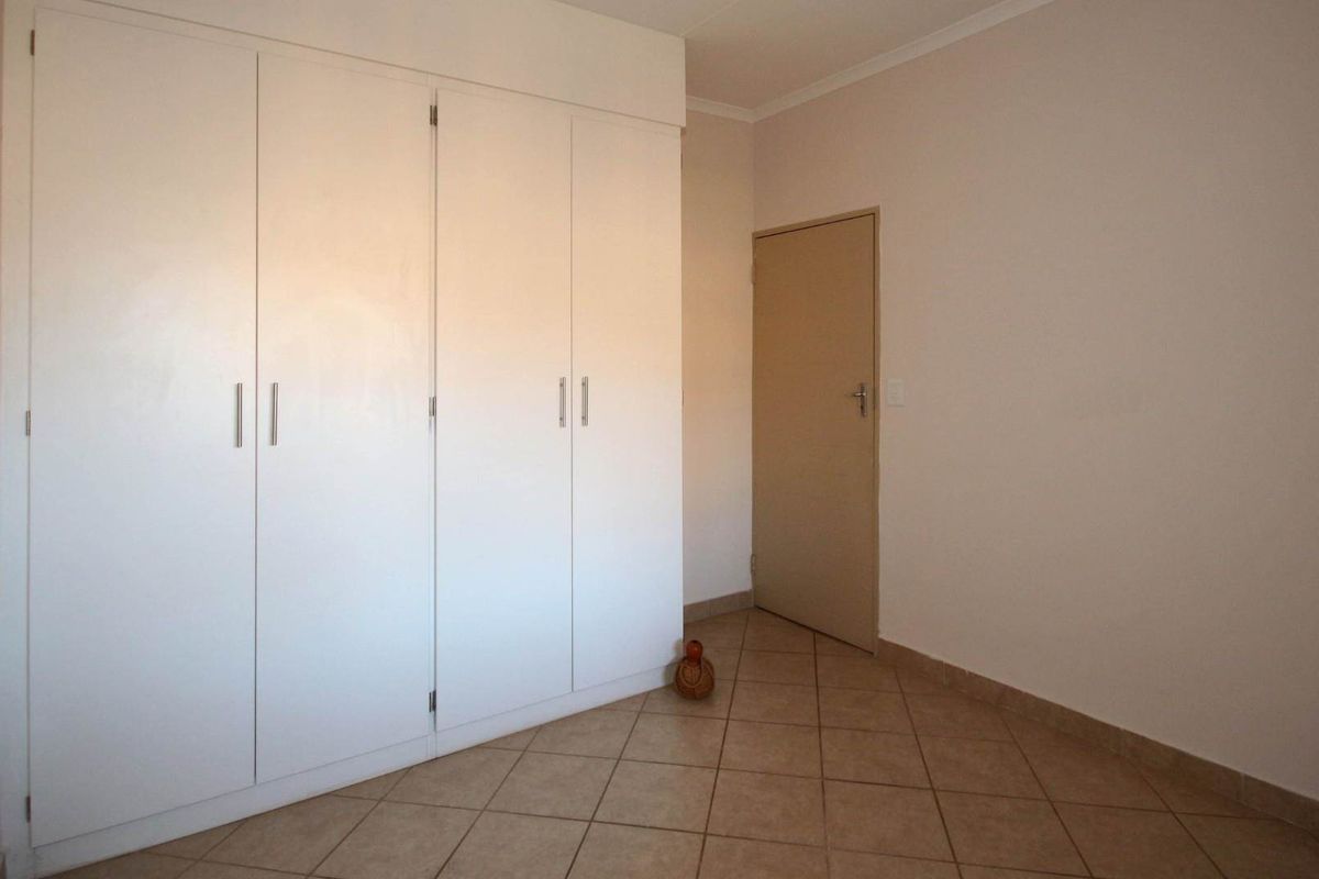 A clean, empty bedroom featuring neutral tiled flooring and ample built-in cupboard storage space.