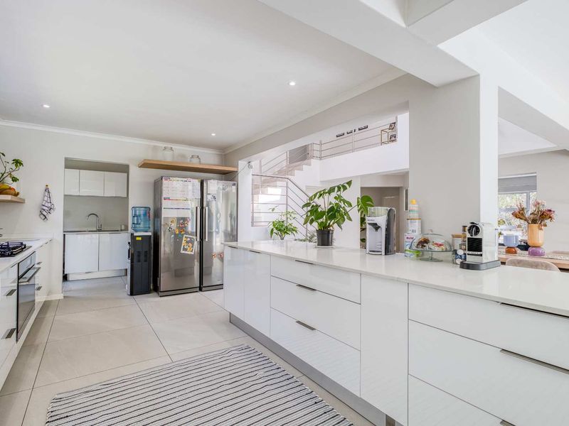 Modern open-plan kitchen featuring a large central island, sleek white cabinetry, stone countertops, and integrated appliances, flowing into the living area.
