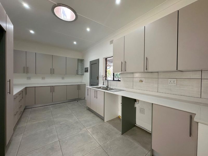 A modern, clean kitchen featuring extensive built-in cabinetry, stone countertops, tiled flooring, and a skylight, providing a bright and functional workspace.