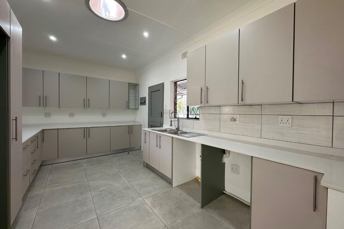 A modern, clean kitchen featuring extensive built-in cabinetry, stone countertops, tiled flooring, and a skylight, providing a bright and functional workspace.
