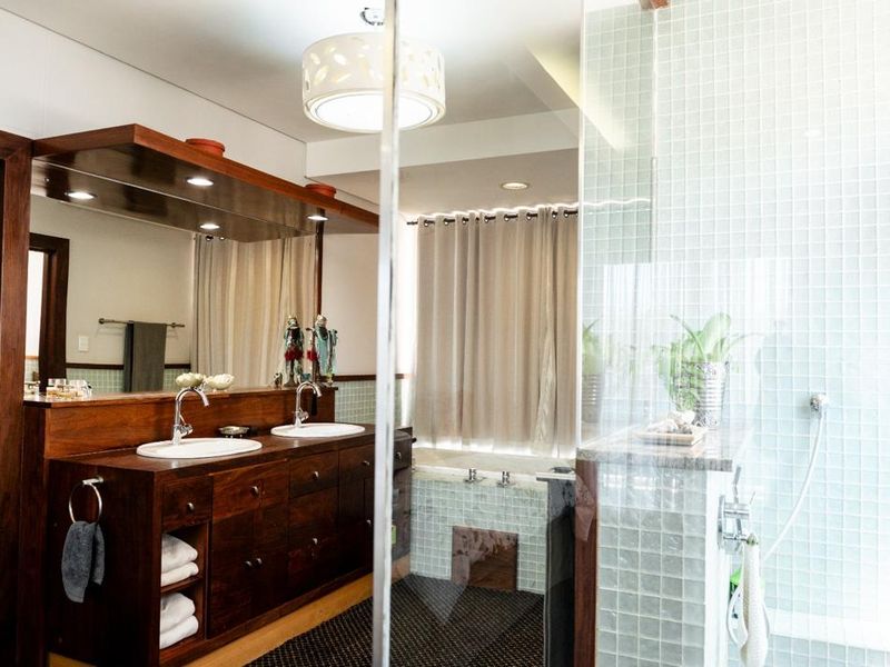 Spacious bathroom featuring a dark wood double vanity with dual sinks, a large mirror, a glass-enclosed shower with mosaic tiling, and a built-in bathtub.
