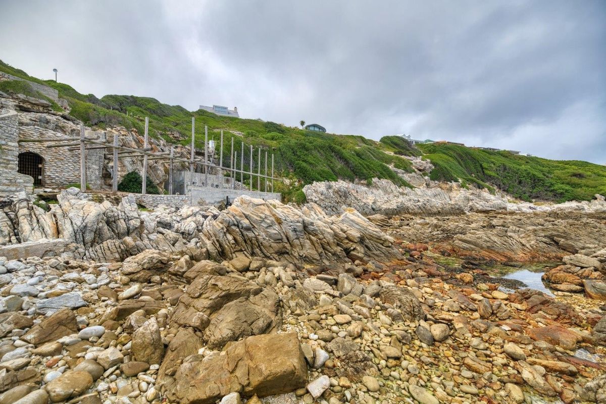 Coastal vacant land featuring rugged rocky terrain and an incomplete stone and timber structural framework set against a hillside landscape.