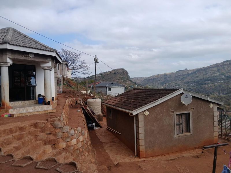 Rear view of the property showing multiple structures, stone retaining walls, and a scenic hilly landscape backdrop.