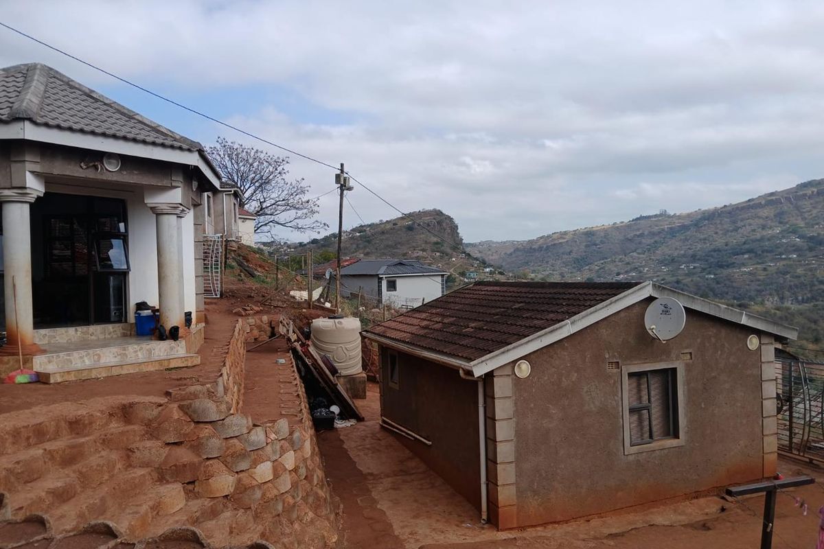 Rear view of the property showing multiple structures, stone retaining walls, and a scenic hilly landscape backdrop.