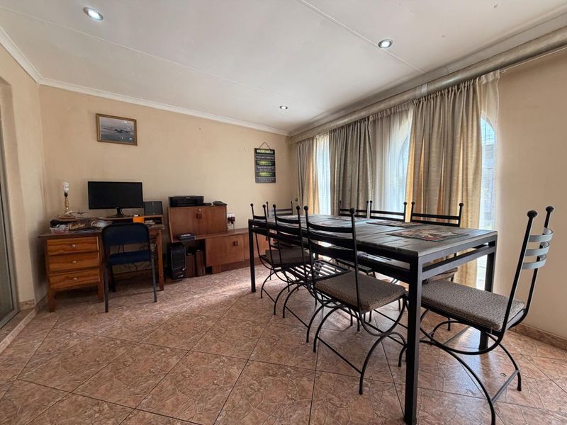 A functional dining room featuring tiled flooring and recessed downlights, currently utilized as a combined dining and workspace area.