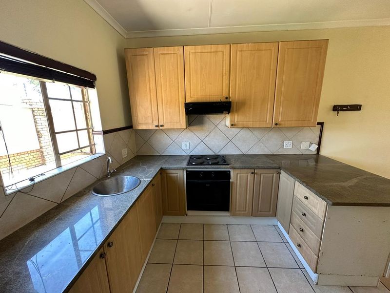 Functional kitchen featuring granite countertops, built-in oven and hob, extractor fan, and ample wooden cabinetry with tiled flooring and backsplash.