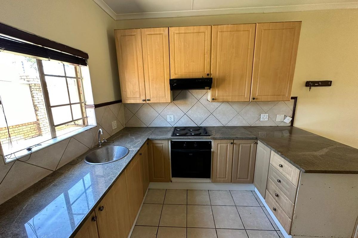 Functional kitchen featuring granite countertops, built-in oven and hob, extractor fan, and ample wooden cabinetry with tiled flooring and backsplash.