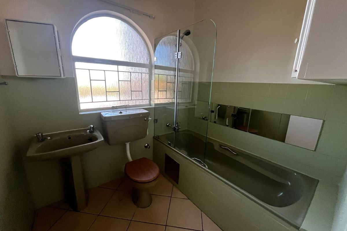 A dated bathroom featuring a pedestal basin, toilet, and a bathtub with a glass shower screen, finished with tiled walls and flooring.