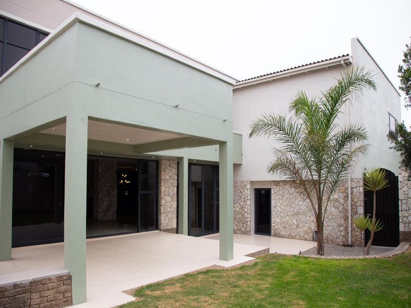 Rear view of the property featuring a covered patio with stone cladding, large sliding glass doors, and a well-maintained garden area.