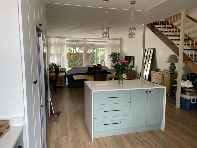 Spacious open-plan living area featuring a modern kitchen island, timber-look flooring, and a staircase, flowing seamlessly to the rear garden through sliding glass doors.