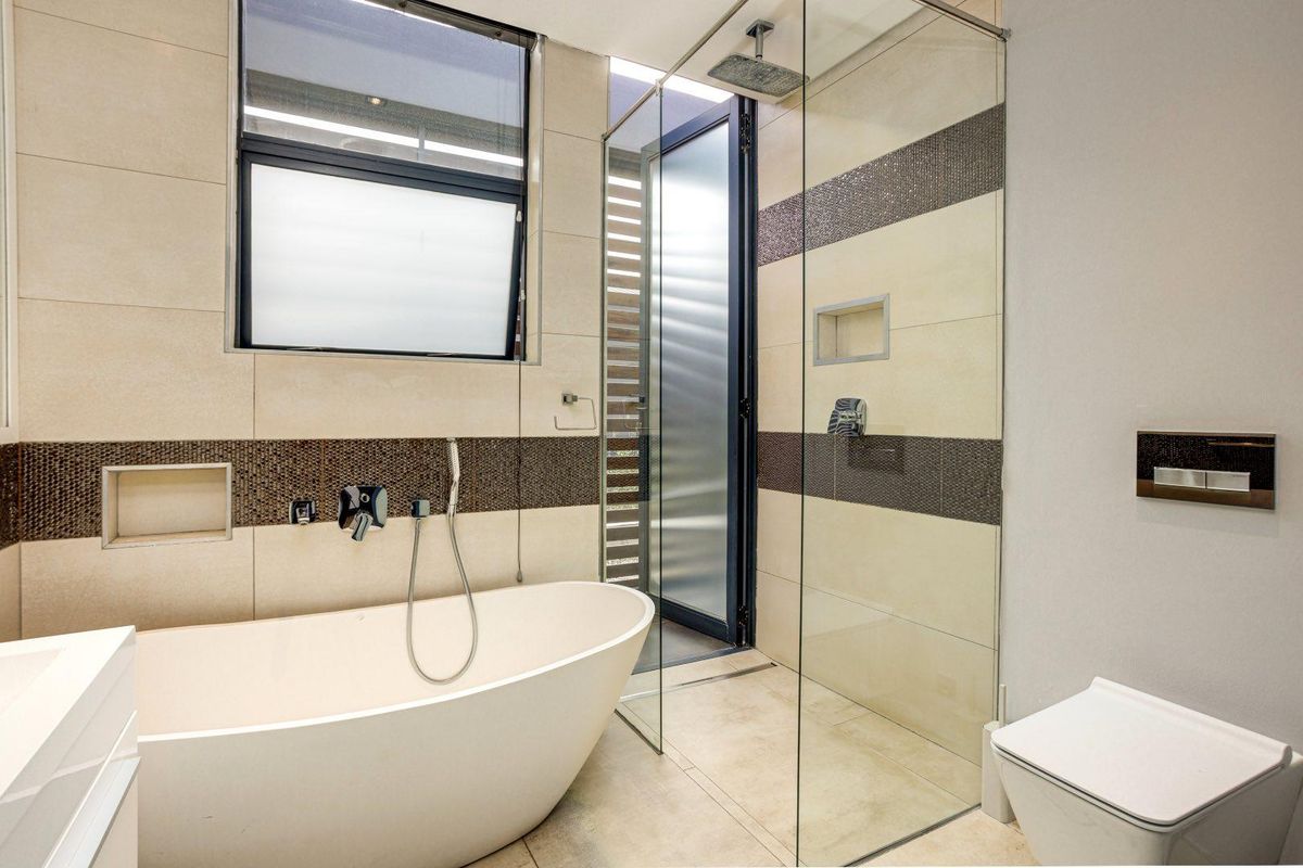 Modern bathroom featuring a freestanding bathtub, glass-enclosed walk-in shower with rainfall showerhead, wall-mounted toilet, and contemporary tiled finishes.