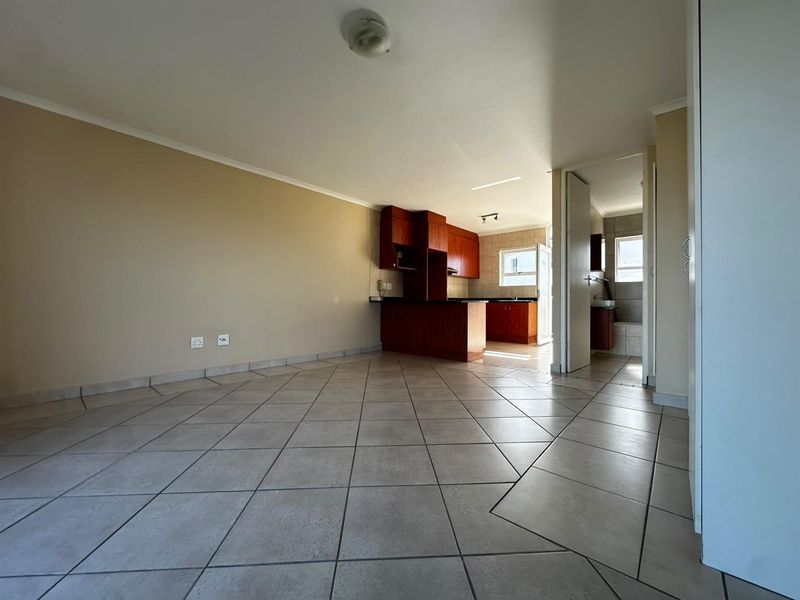 An open-plan living area featuring tiled flooring and a connected kitchen with wooden cabinetry, offering a functional and versatile layout.