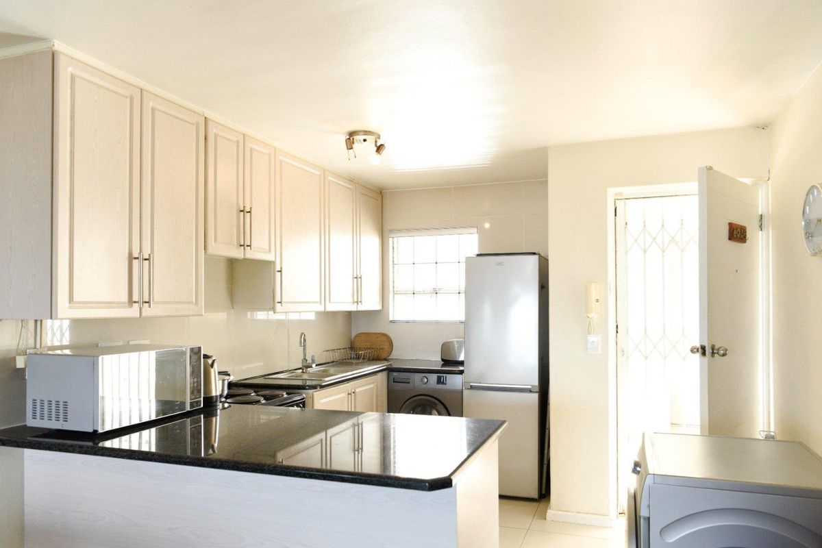 A functional kitchen featuring light-toned cabinetry, dark granite countertops, a stainless steel sink, and integrated space for laundry appliances.