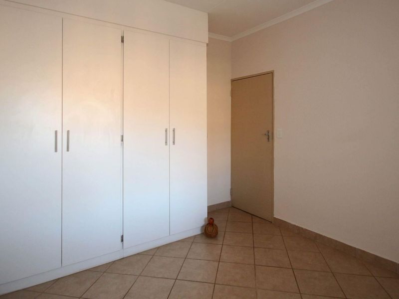 A clean, empty bedroom featuring neutral tiled flooring and ample built-in cupboard storage space.