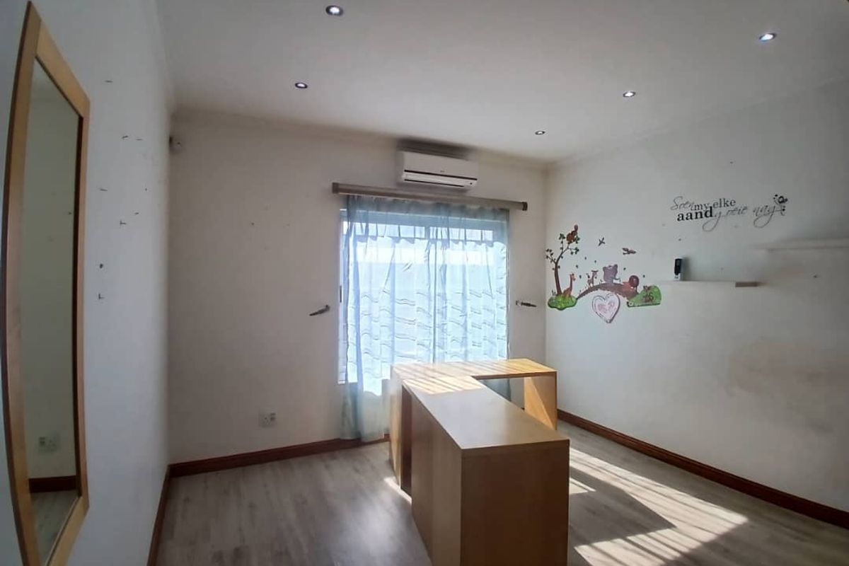 A bedroom featuring laminate flooring, recessed downlighting, and a wall-mounted air conditioning unit, currently used as a workspace.