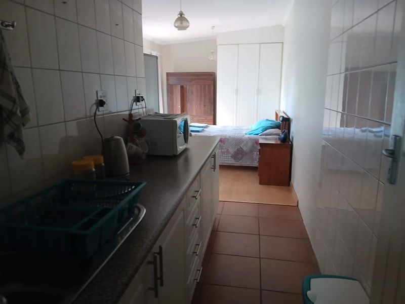 A compact open-plan studio space featuring a kitchenette with built-in cabinetry and tiled splashbacks, seamlessly transitioning into a bedroom area.