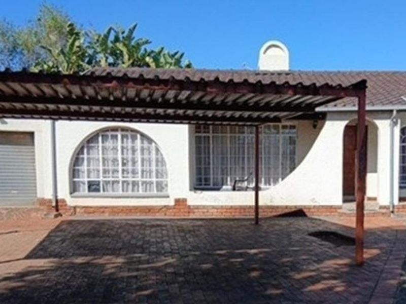 Front elevation of the property featuring a paved driveway, a metal carport, and arched window detailing with a tiled roof.