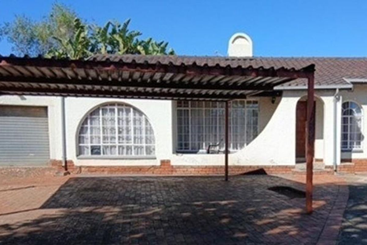 Front elevation of the property featuring a paved driveway, a metal carport, and arched window detailing with a tiled roof.