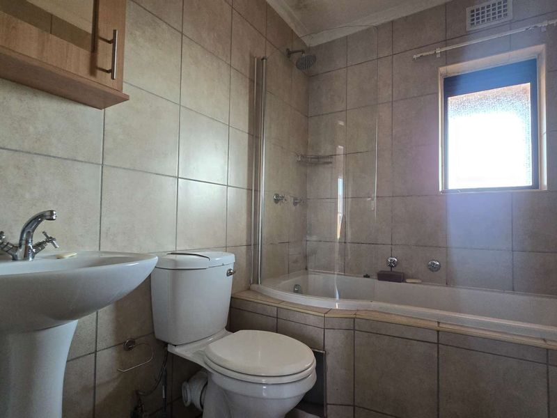 A functional bathroom featuring a pedestal basin, toilet, and a bathtub with an integrated shower and glass screen, finished with neutral wall tiles.