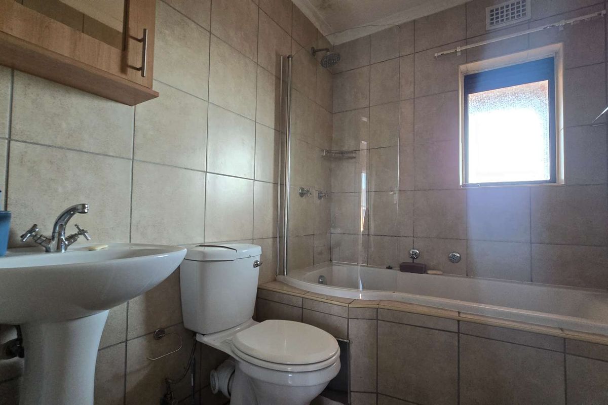 A functional bathroom featuring a pedestal basin, toilet, and a bathtub with an integrated shower and glass screen, finished with neutral wall tiles.