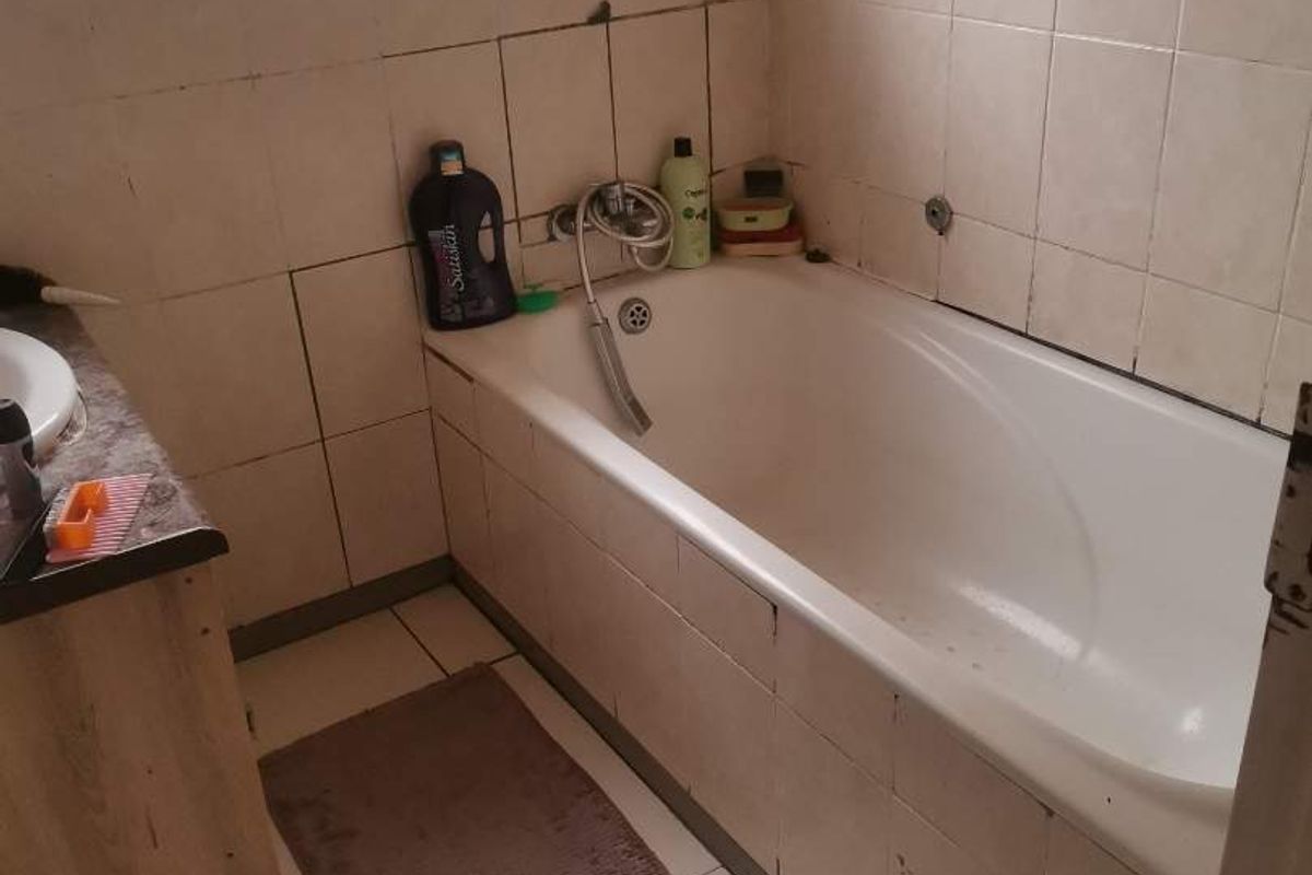 A compact bathroom featuring a built-in bathtub, tiled walls, and a vanity unit with a basin, situated under a window with security bars.