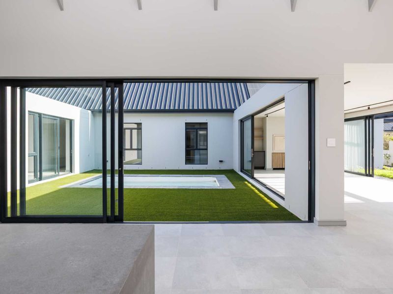 Modern open-plan living area featuring large sliding glass doors that open onto a central courtyard with a plunge pool and artificial lawn.