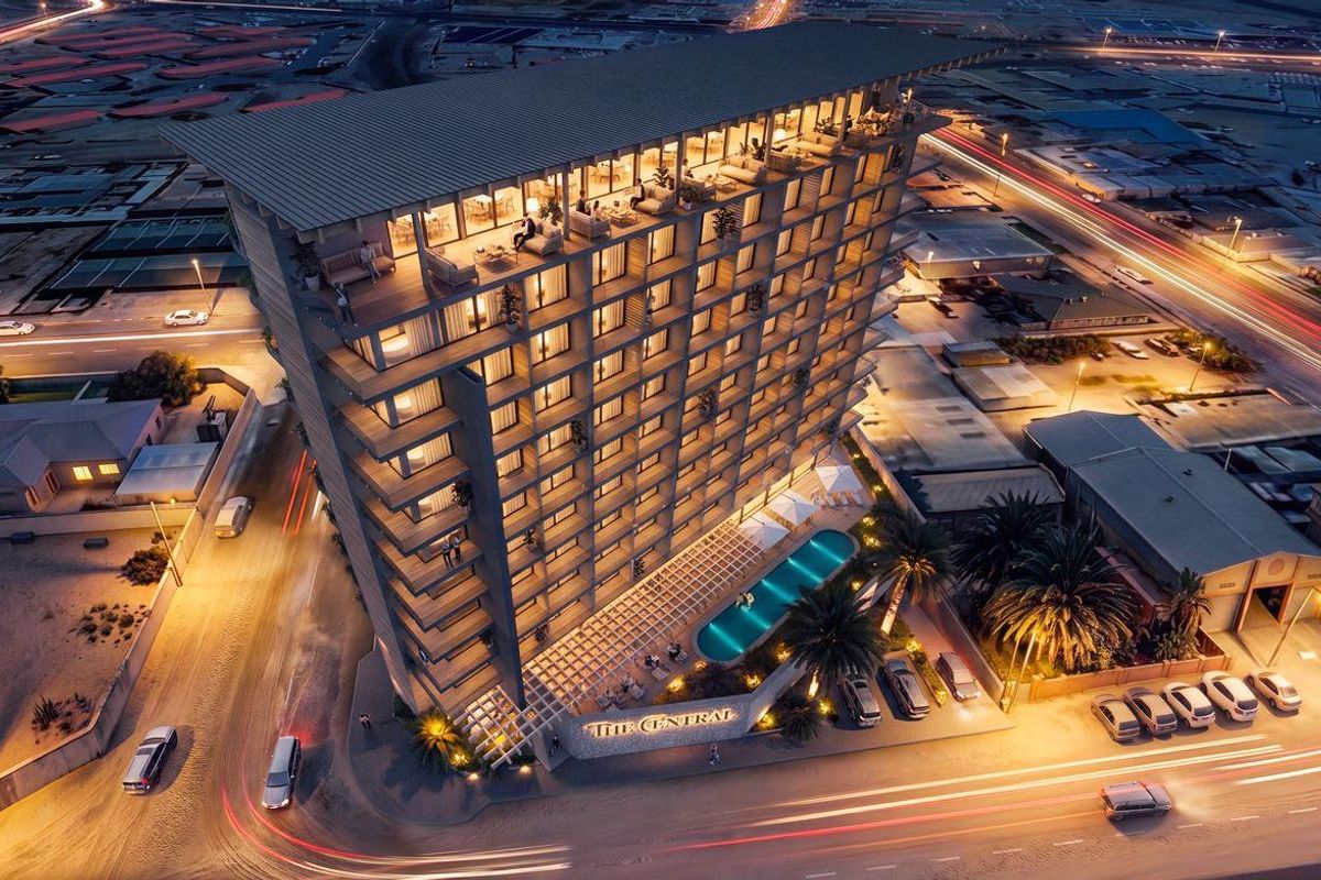 Aerial view of The Central apartment building at night, featuring modern architecture, a ground-level swimming pool, and surrounding urban infrastructure.