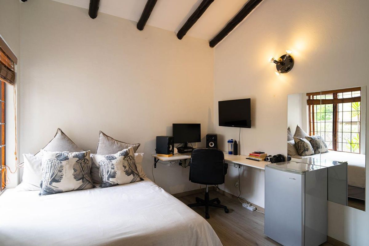 A bedroom featuring exposed timber ceiling beams, a built-in desk area, and a large window with wooden blinds.