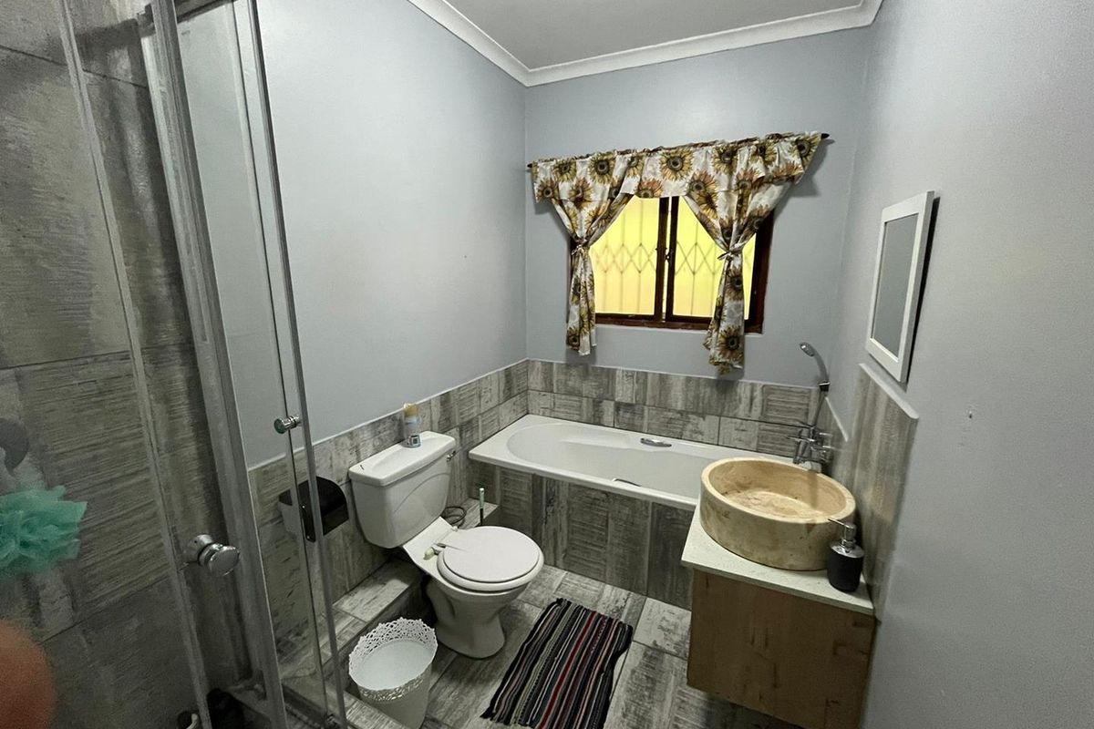 A functional bathroom featuring a built-in bathtub, glass-enclosed shower, vessel sink vanity, and neutral tiled finishes.