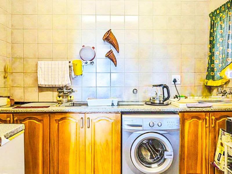 A functional laundry area featuring built-in wooden cabinetry, a stainless steel sink, and tiled splashbacks, providing practical utility space.